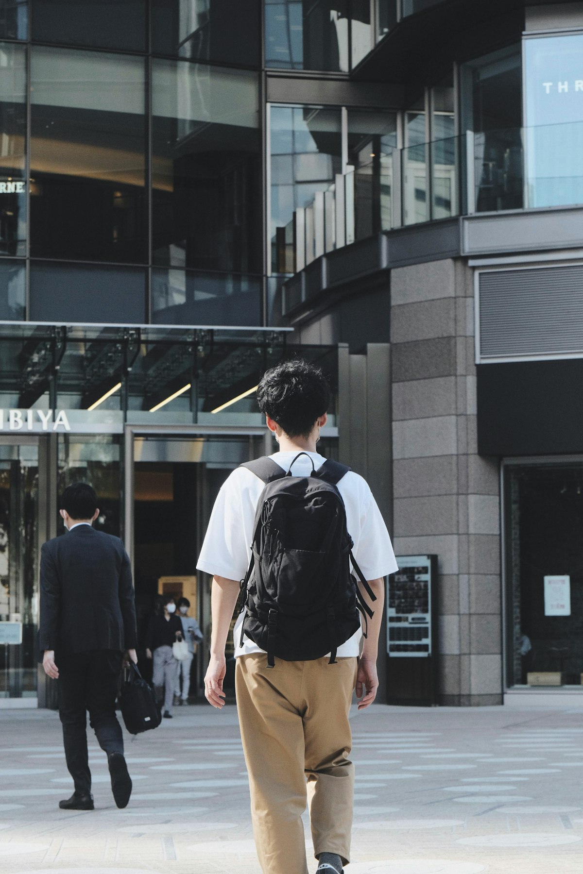 オフィスビルへ向かうリュック姿の若者の後ろ姿